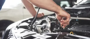 Mechanic working under the hood of a vehicle needing repairs.
