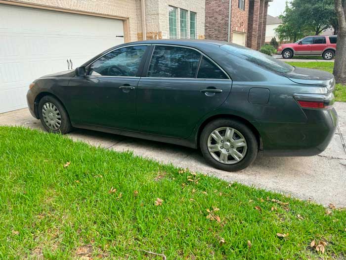 Toyota Camry 2010 Dark sedan parked on a suburban driveway in Cinco Ranch, TX, ready to be sold for cash to Junk Car Buyers R-Us.