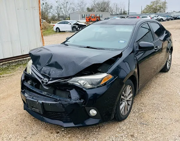 Severely damaged front end of a black Toyota Corolla at a salvage yard, ready for pickup by Junk Car Buyers R-Us in Porter, TX.