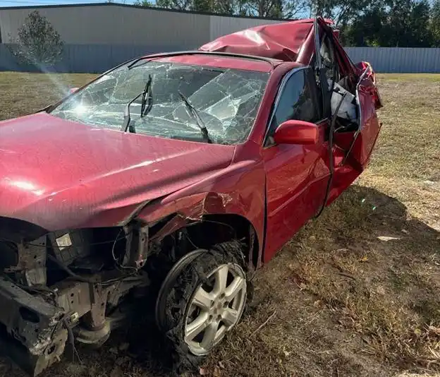 Carro rojo con daños severos en el techo, parabrisas y parte frontal.