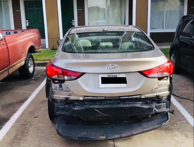 Rear view of a damaged beige Hyundai Elantra parked at an apartment complex.