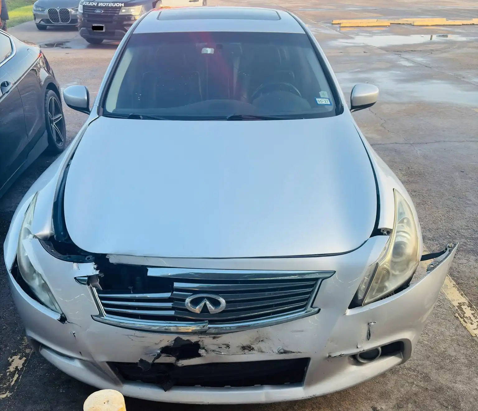 Silver Infiniti sedan with visible front-end collision damage parked outdoors.