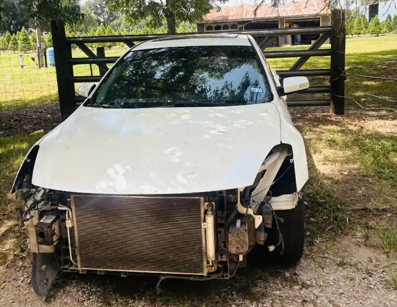 Damaged white car with front-end parts missing before evaluation by Junk Car Buyers-R-Us.