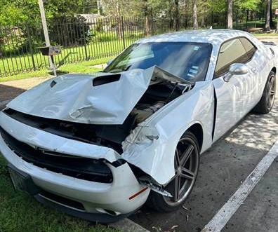 Dodge Challenger blanco con fuertes daños frontales estacionado en League City, TX.