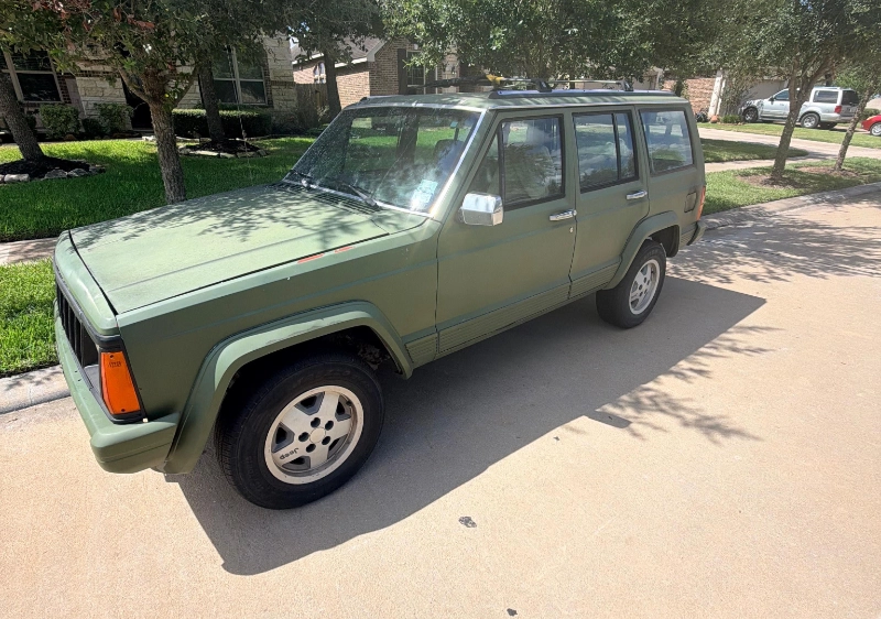 Older green Jeep Cherokee parked before sale in Porter, Texas.
